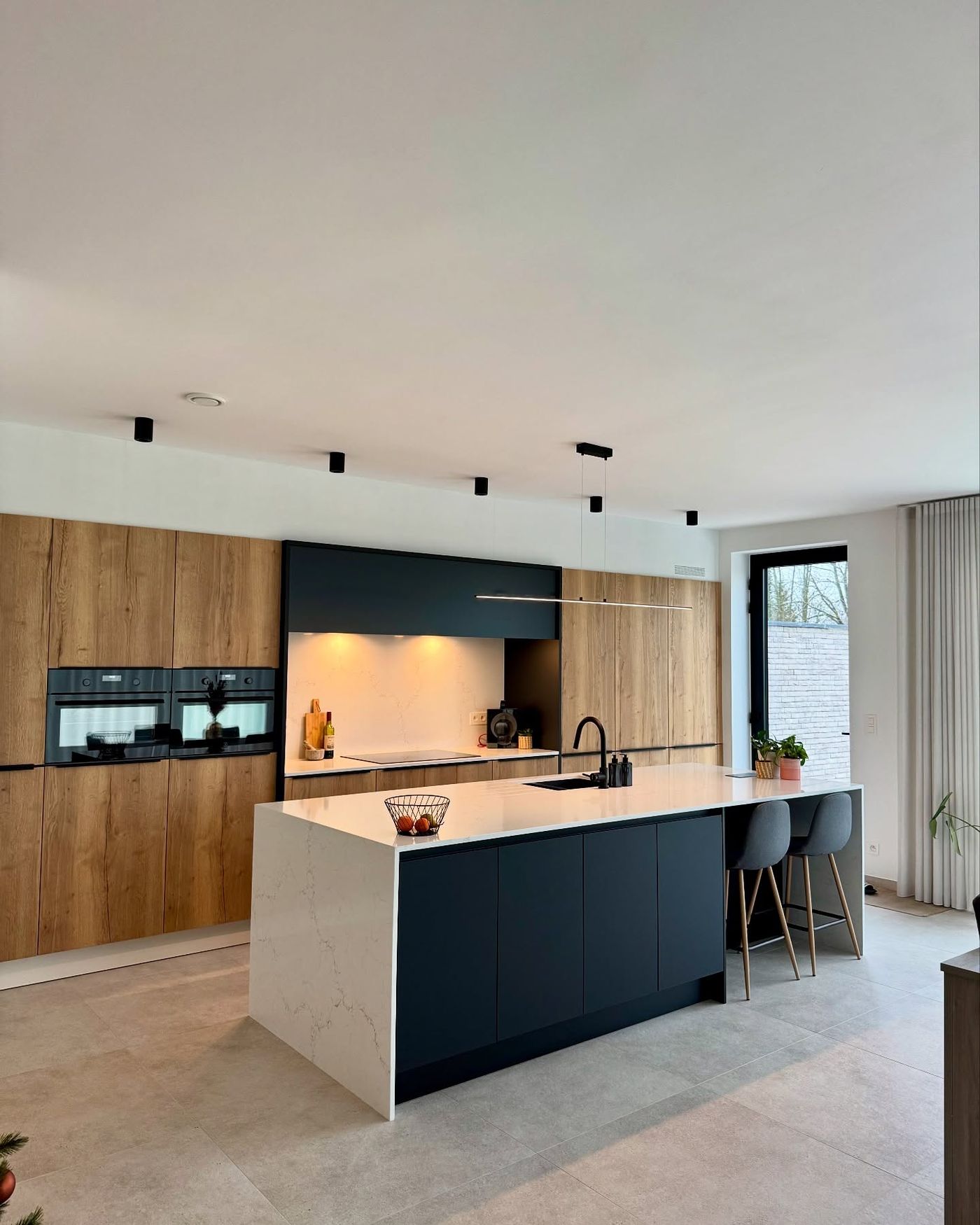 Hedendaagse keuken met donkerblauw eiland, eiken kasten en composieten werkblad
